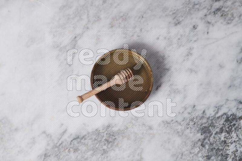 Multicolored pottery oven plate with wooden honey dipper in it on grey marble background