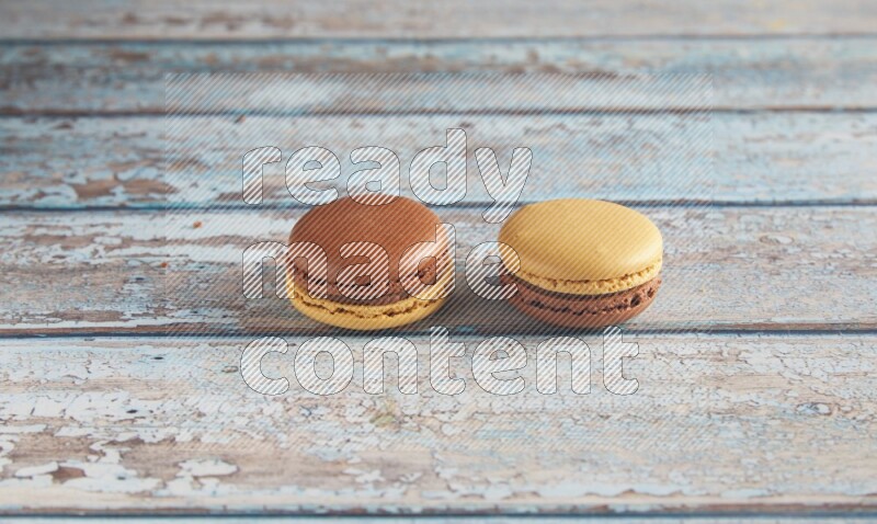 45º Shot of two Yellow and Brown Chai Latte macarons on light blue wooden background