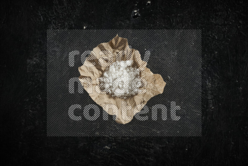 A crumpled piece of paper full of white salt on black background