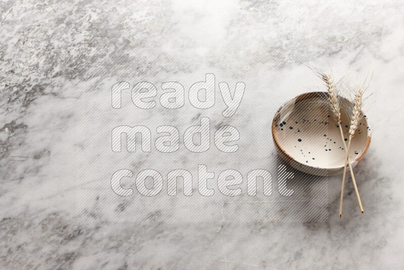 Wheat stalks on multicolored pottery bowl on grey marble background