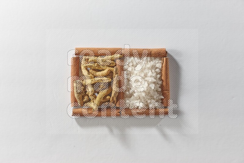 مربعان من أعواد القرفة ممتلئان بأصابع الكركم والملح الأبيض علي خلفية بيضاء