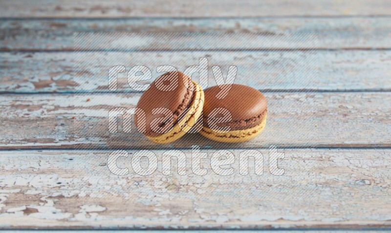 45º Shot of two Yellow and Brown Chai Latte macarons on light blue wooden background