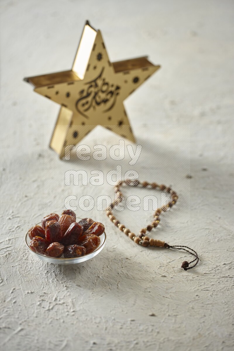 A wooden golden star lantern with different drinks, dates, nuts, prayer beads and quran on textured white background