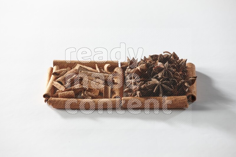 مربعان من أعواد القرفة ممتلئان باليانسون النجمي وقطع من القرفة علي خلفية بيضاء