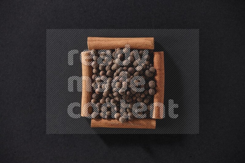 A single square of cinnamon sticks full of allspice on black flooring
