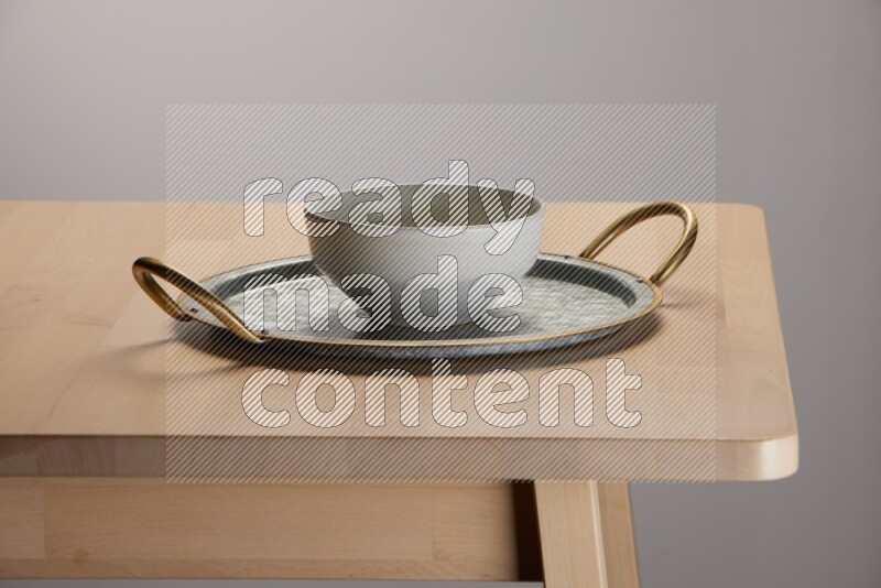 grey bowl placed on a rounded stainless steel tray with golden handels on the edge of wooden table