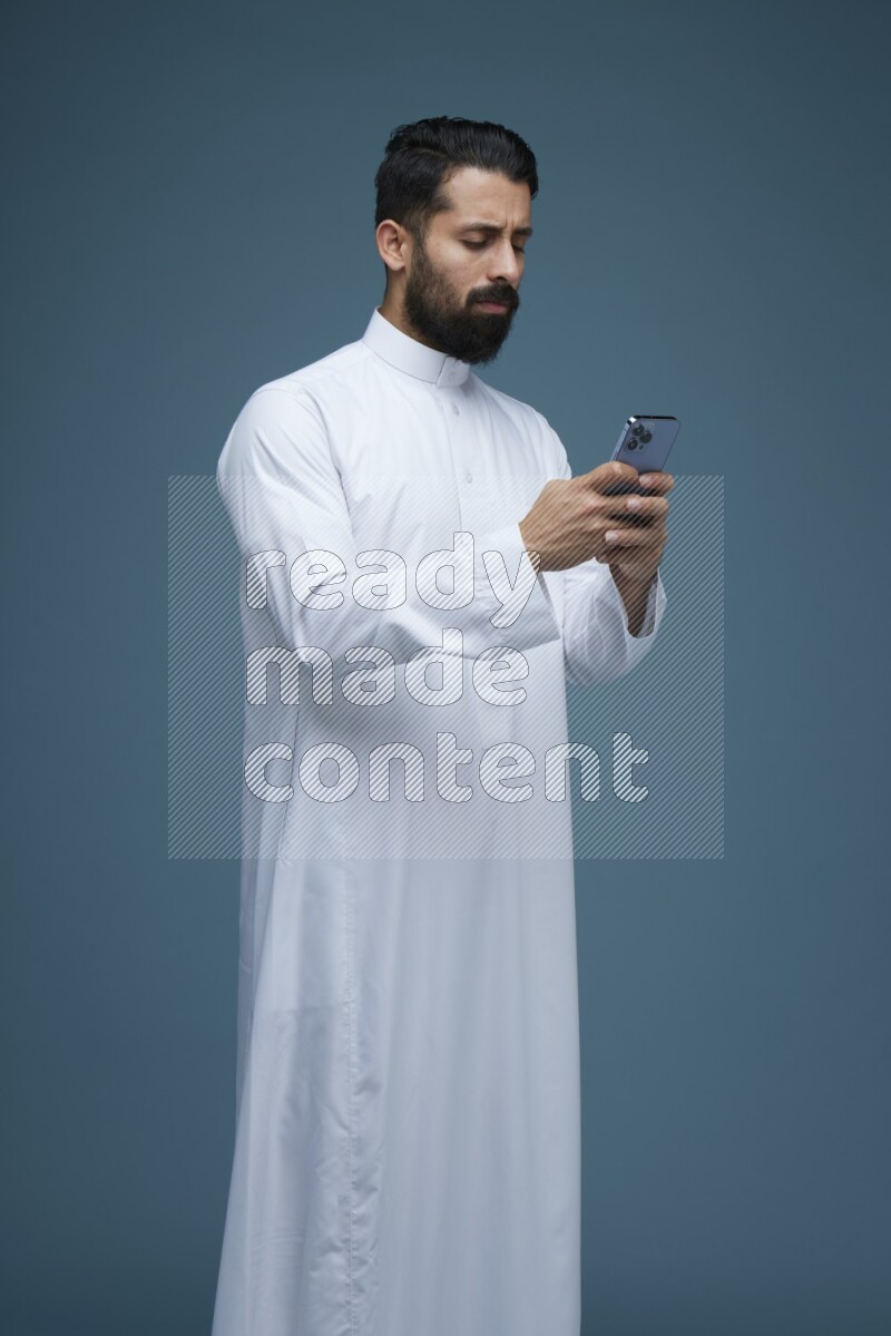 A man Texting in a blue background wearing Saudi Thob
