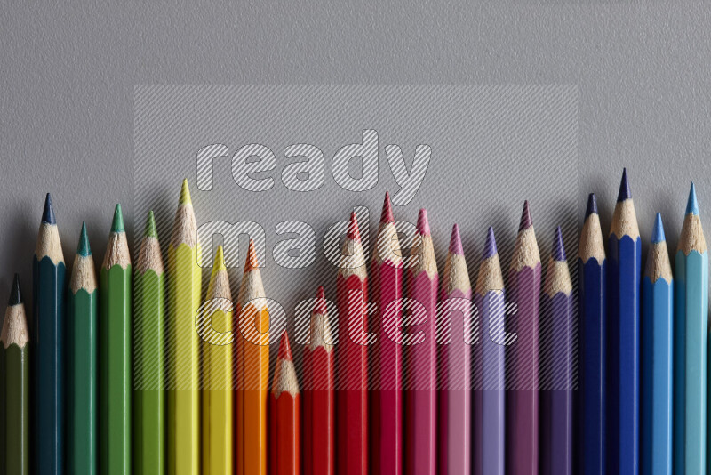A collection of colored pencils arranged showcasing a gradient of different hues on grey background