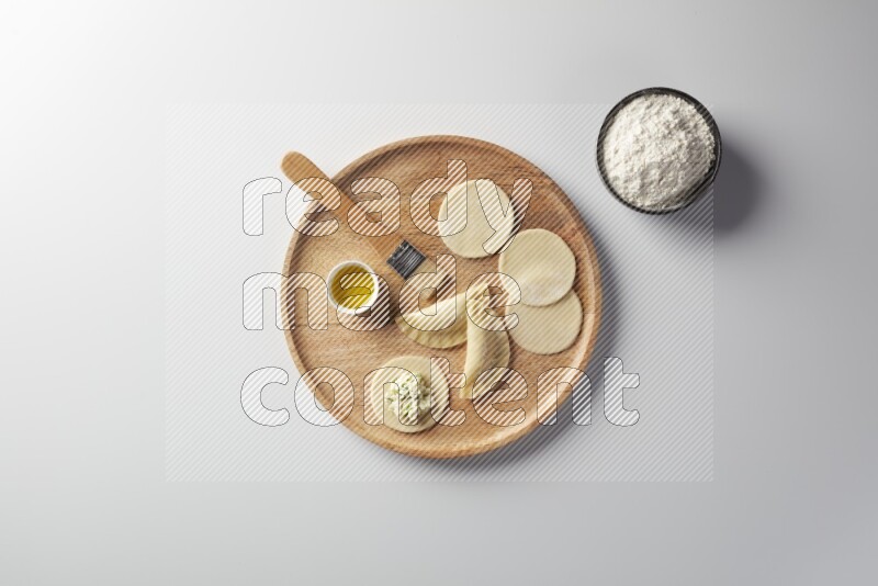 two closed sambosas and one open sambosa filled with cheese while flour, and oil with oil brush aside in a wooden dish on a white background