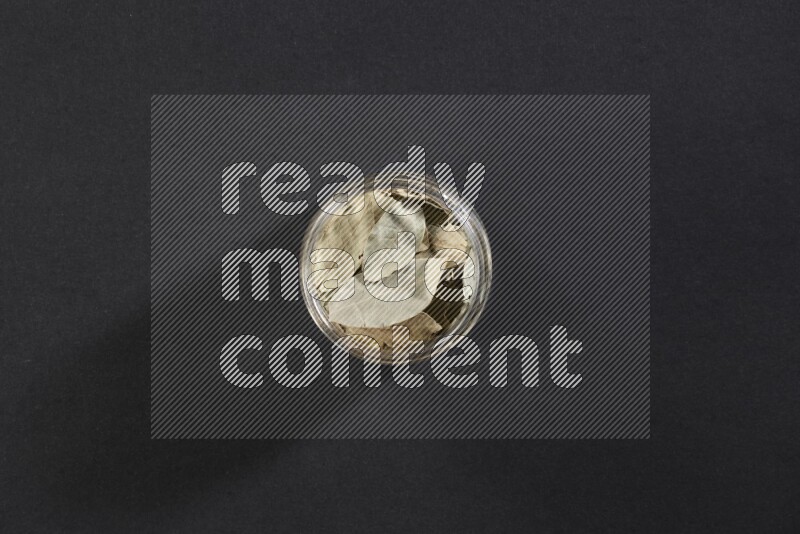 A glass jar filled with dried bay leaves on black flooring