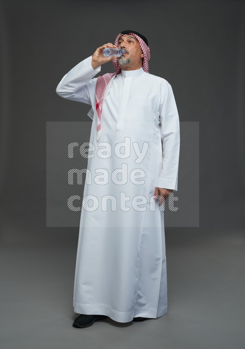 Saudi man with shomag Standing drinking water on gray background