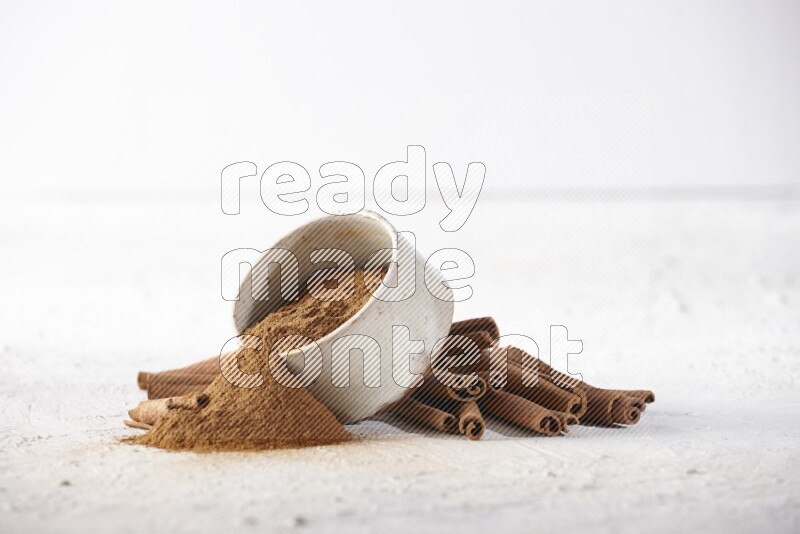 Ceramic beige bowl over filled with cinnamon powder and cinnamon sticks around the bowl on a textured white background in different angles