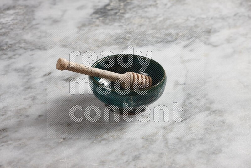 Dark green pottery plate with wooden honey dipper in it on grey marble background