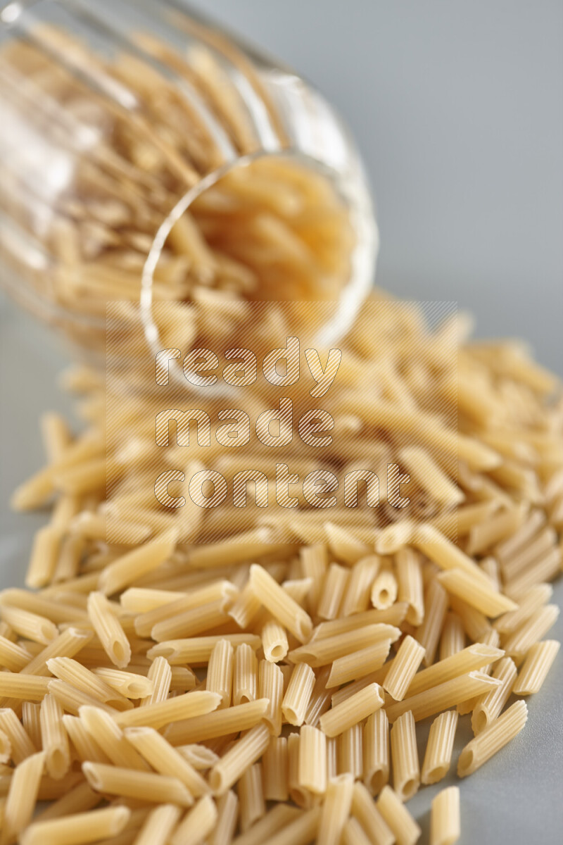 Flipped jar full of raw pasta on light blue background