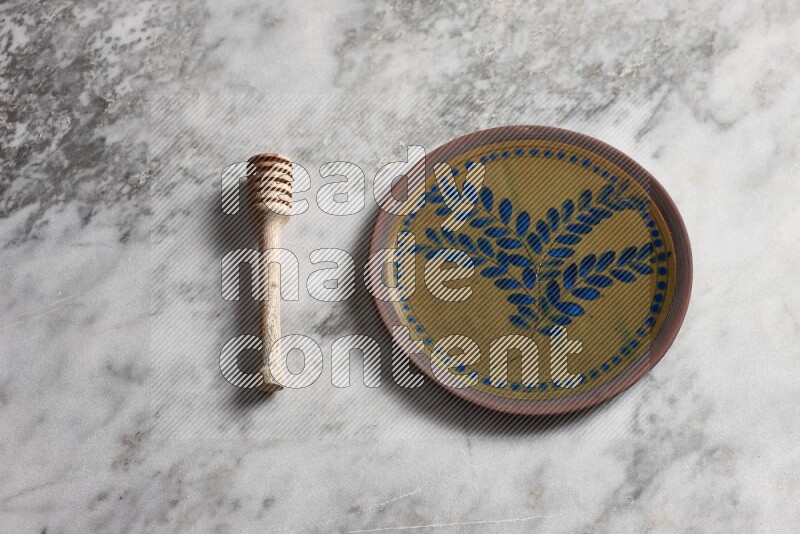 Decorative pottery plate with wooden honey dipper on the side on grey marble background