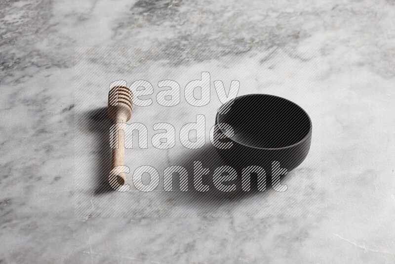 Black pottery bowl with wooden honey dipper on the side on grey marble background