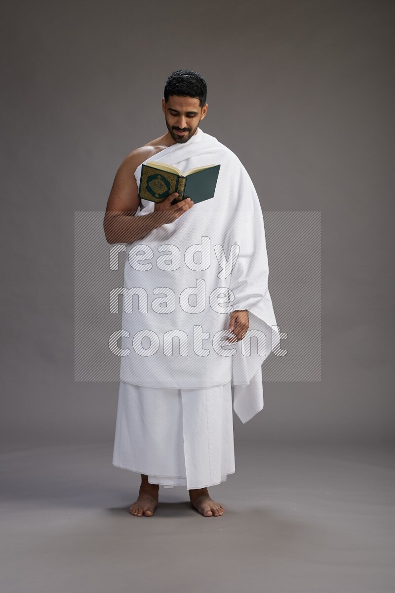 A man wearing Ehram Standing reading quran on gray background