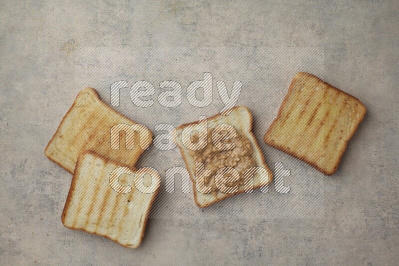 Crunchy peanut butter on a toasted white toast and toasted white toast slices on a light blue textured background