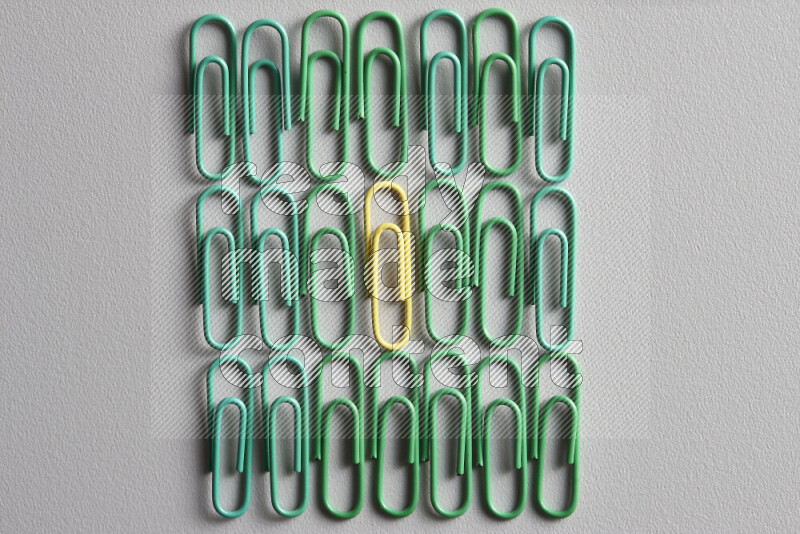A bunch of green paper clips with a different colored paper clip in the center on grey background