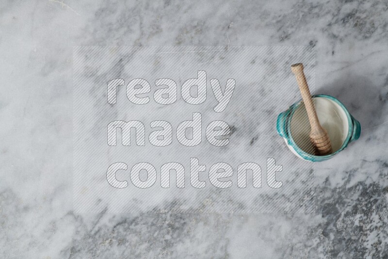 Multicolored pottery bowl with wooden honey dipper in it on grey marble background