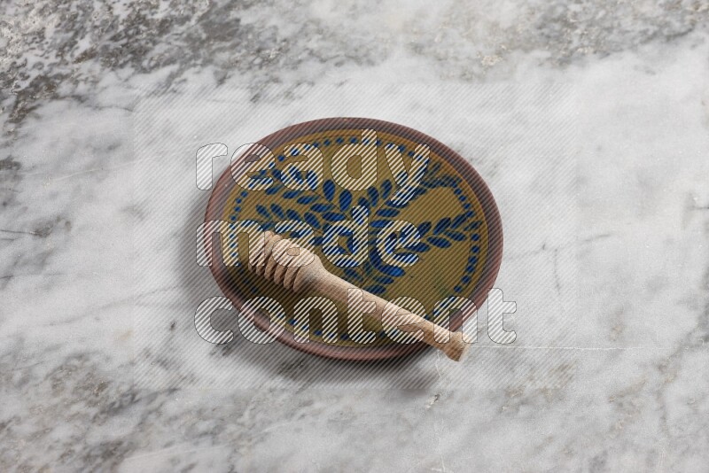 Decorative pottery plate with wooden honey dipper in it on grey marble background