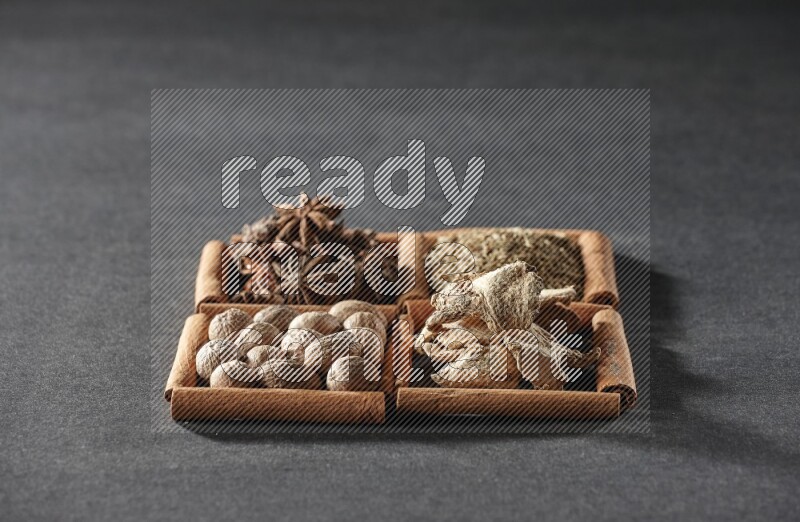 4 مربعات من عيدان القرفة ممتلئة باليانسون النجمي والكمون والزنجبيل المجفف وجوزة الطيب على أرضية سوداء