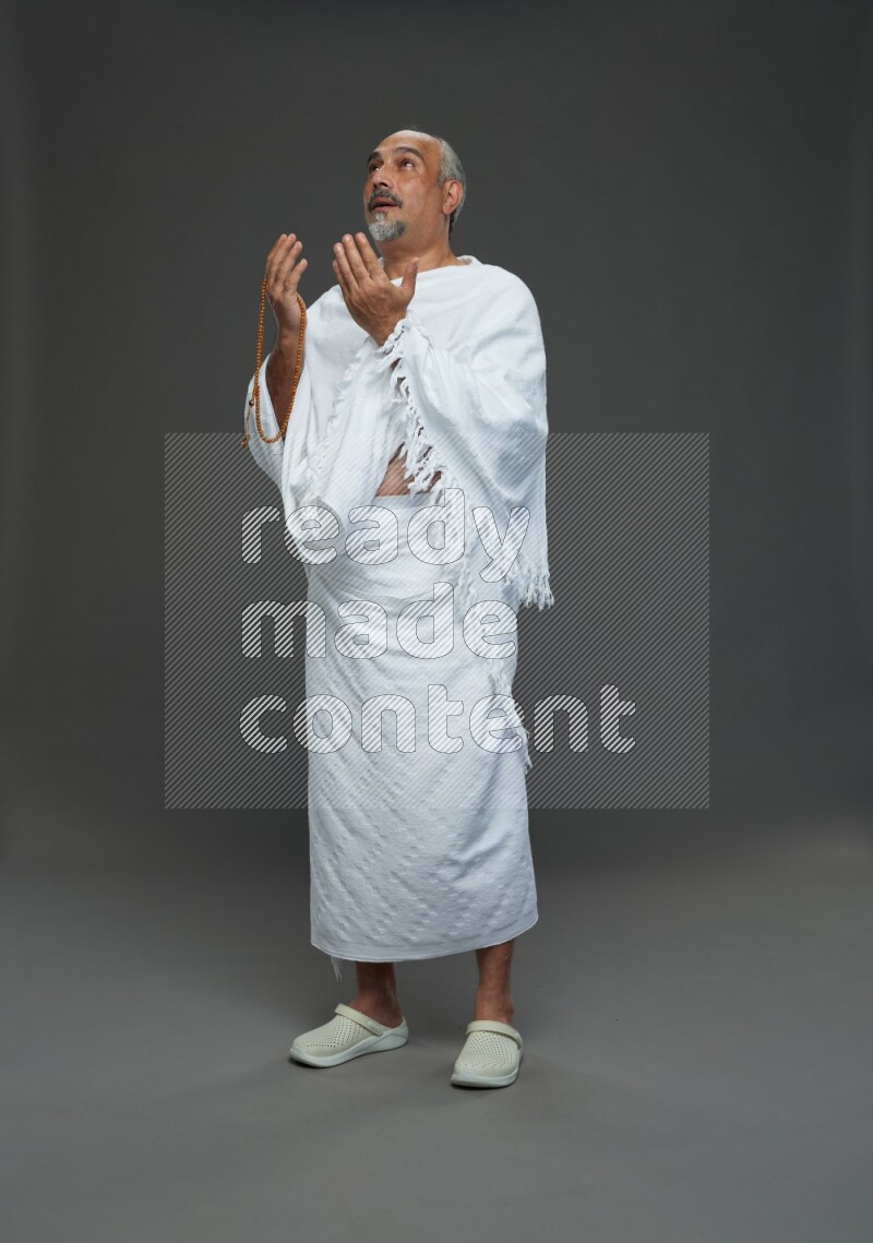 A man wearing Ehram Standing dua'a on gray background