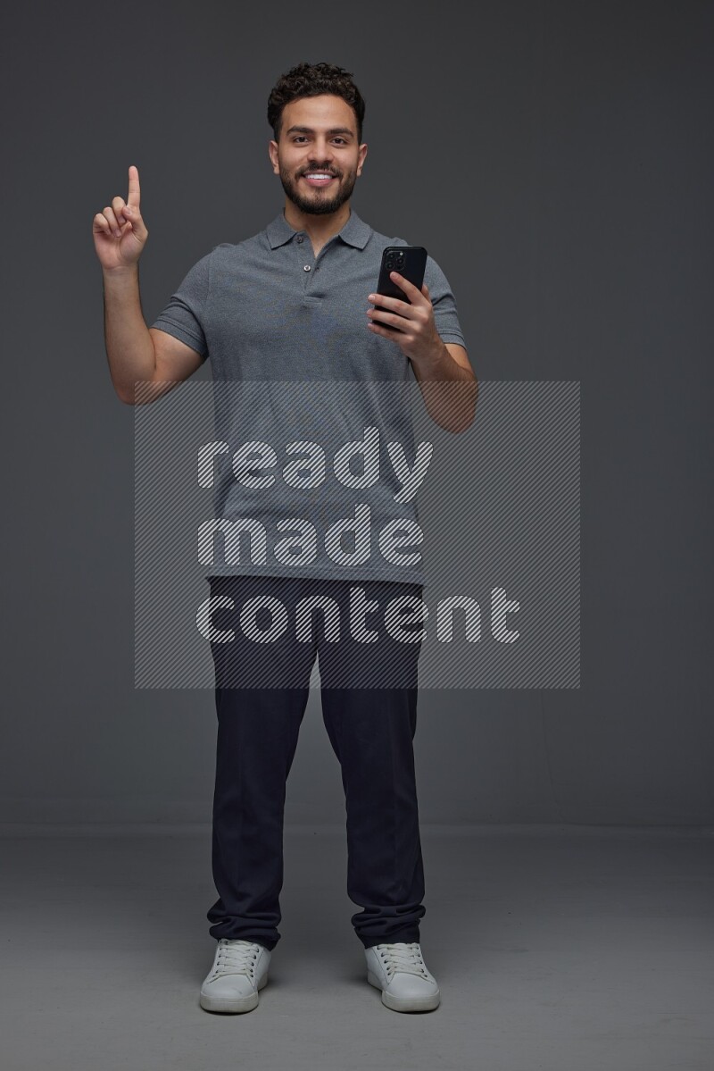 A man wearing casual standing and using his phone and making multi hand gestures eye level on a gray background