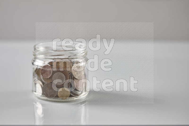 Random old coins in a glass jar on grey background