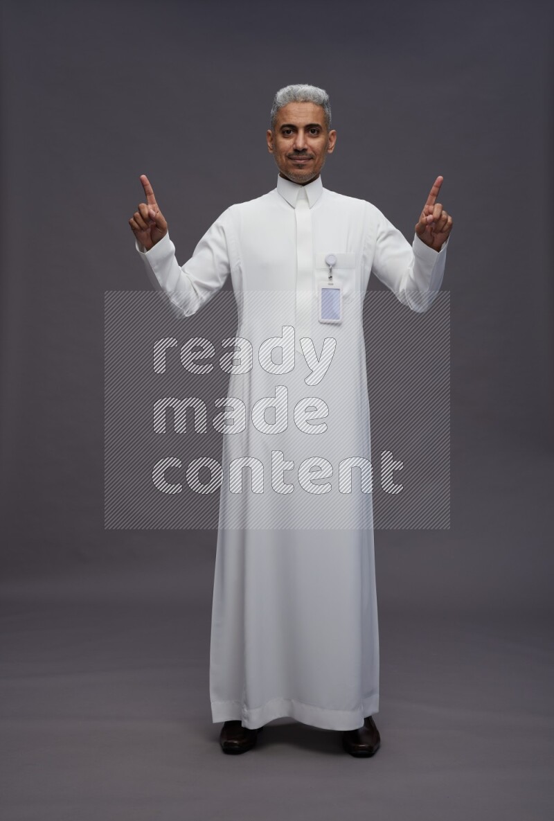 Saudi man wearing thob with pocket employee badge standing interacting with the camera on gray background