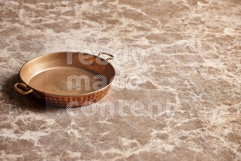 A small copper pan on beige marble background