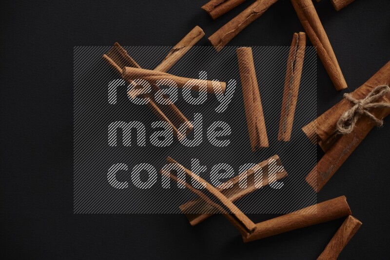 4 Cinnamon sticks stacked and bounded with more sticks in the background on black flooring