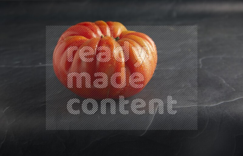 45 degree single heirloom tomato on a textured black slate background