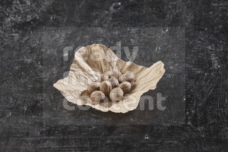 A crumpled piece of paper full of whole nutmeg seeds on a textured black flooring