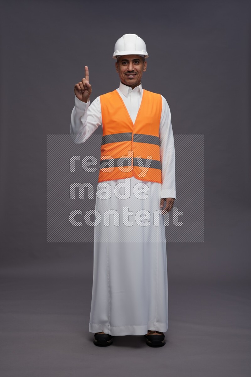 Saudi man wearing thob with engineer vest standing interacting with the camera on gray background