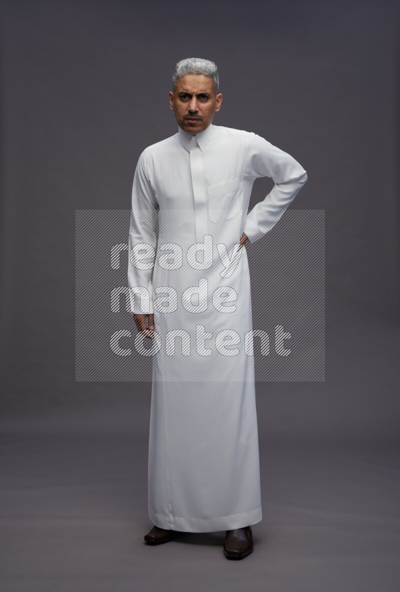 Saudi man wearing thob standing interacting with the camera on gray background