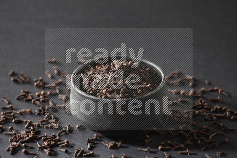A black pottery bowl full of cloves on a black flooring