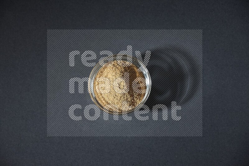 A glass bowl full of cumin powder on black flooring