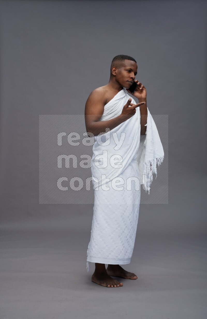 A man wearing Ehram Standing talking on phone on gray background
