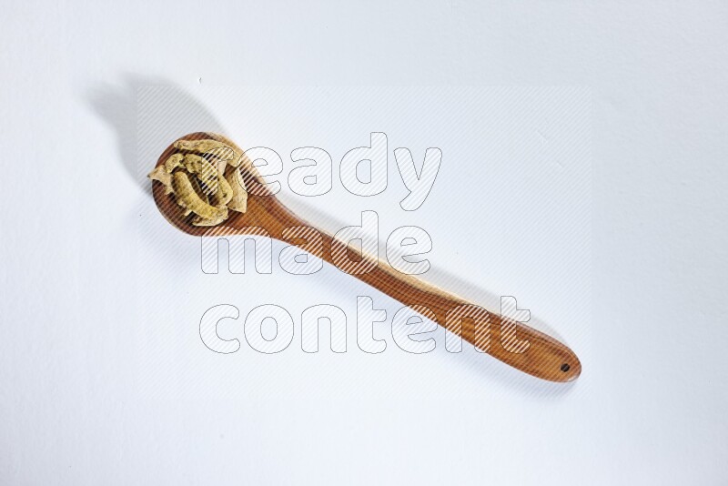 A wooden ladle full of dried turmeric fingers on white flooring