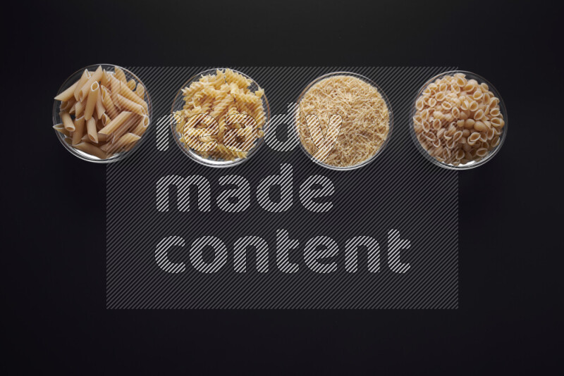 Different pasta types in glass bowls on black background