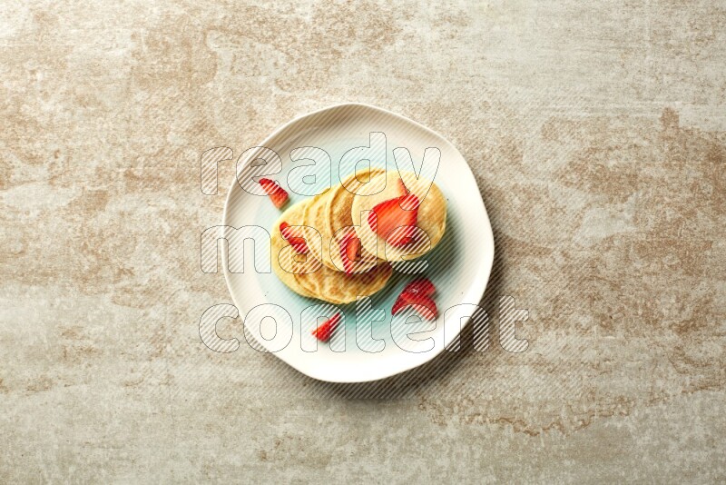 Five stacked strawberry mini pancakes in a bicolor plate on beige background
