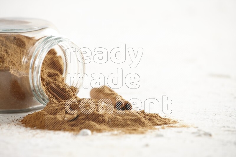 Flipped glass jar full of cinnamon powder with some pieces of cinnamon sticks on a textured white background