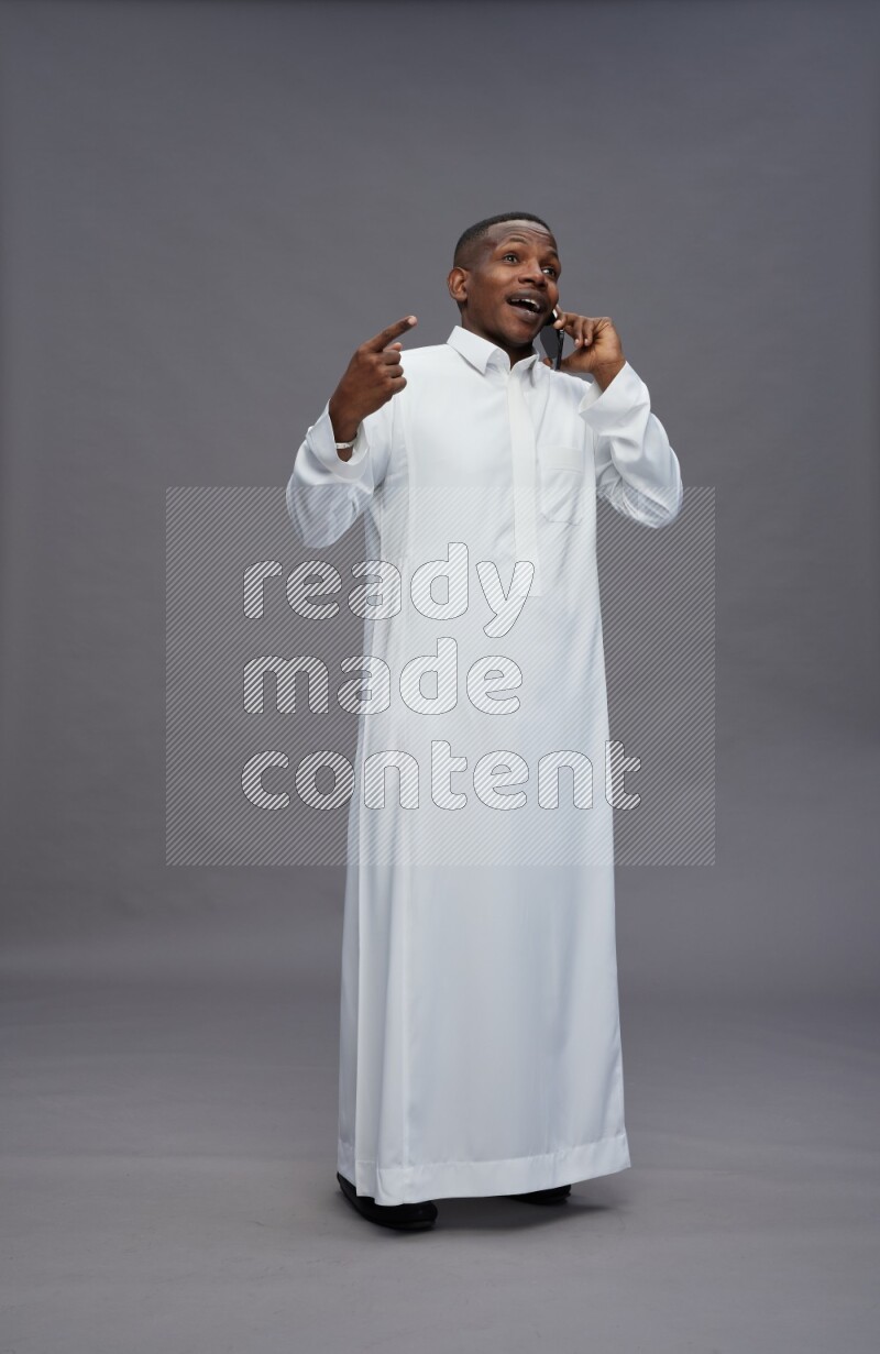 Saudi man wearing thob standing talking on phone on gray background
