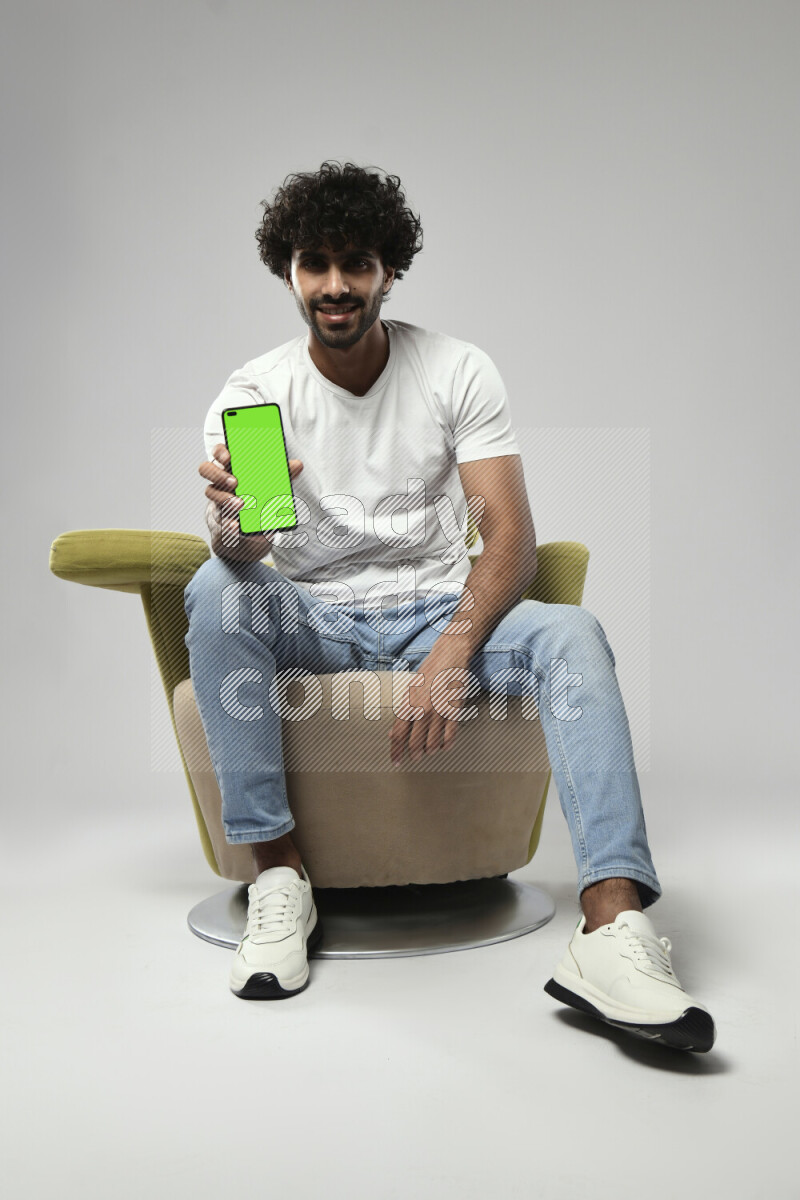 A man wearing casual sitting on a chair showing a phone screen on white background
