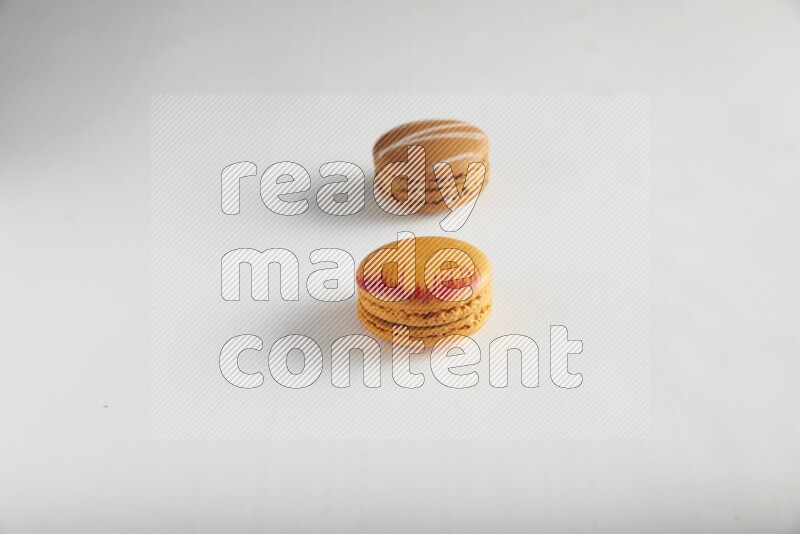 45º Shot of of two assorted Brown Irish Cream, and Orange Exotic macarons on white background