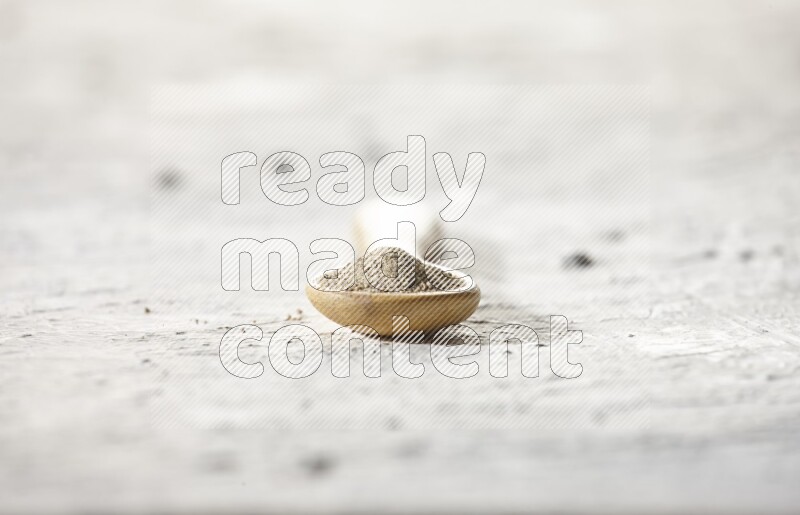 A wooden spoon full of white pepper powder on textured white flooring