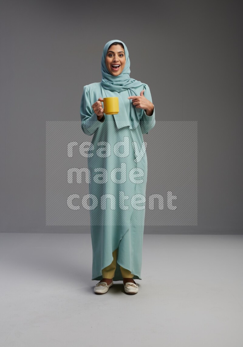 Saudi Woman wearing Abaya standing  holding a mug on Gray background