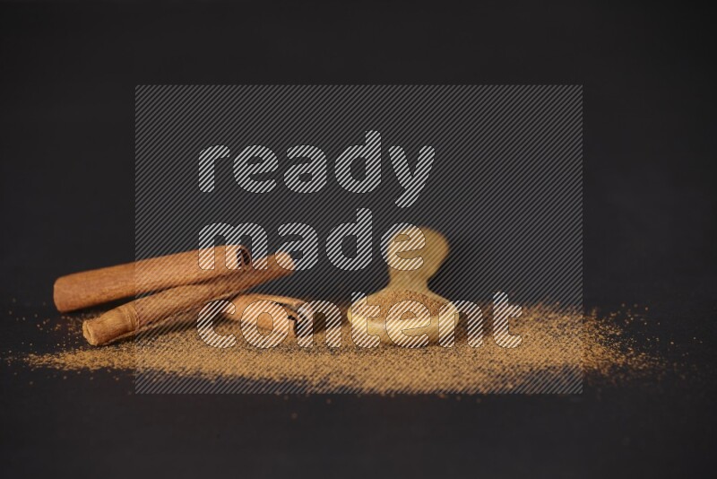 Cinnamon powder in a wooden spoon and cinnamon sticks beside it on black background