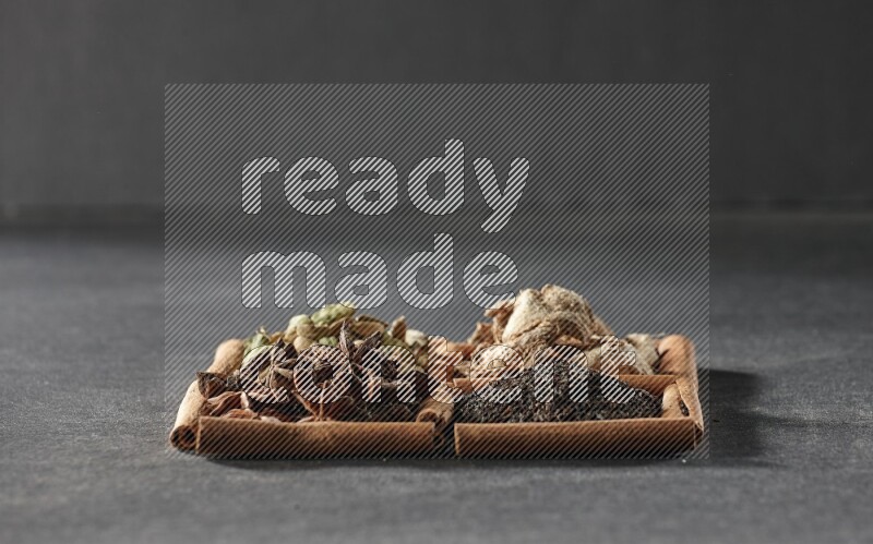 4 مربعات من عيدان القرفة ممتلئة بالشاي واليانسون النجمي والزنجبيل المجفف وحب الهيل على أرضية سوداء